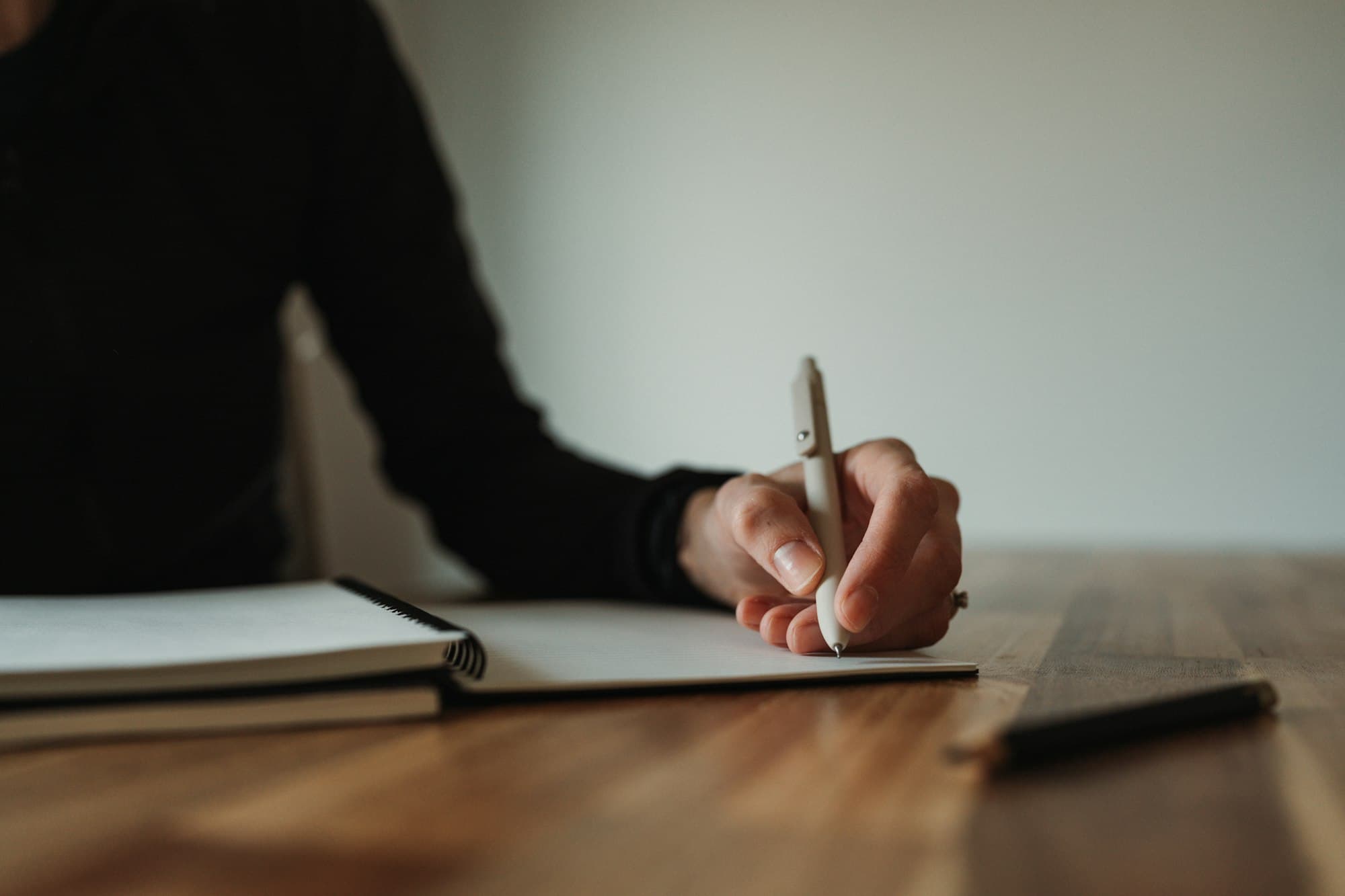 A person writing in a notebook at a wooden desk.